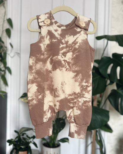 Tie-dye romper with wooden buttons on a hanger with plants in the background