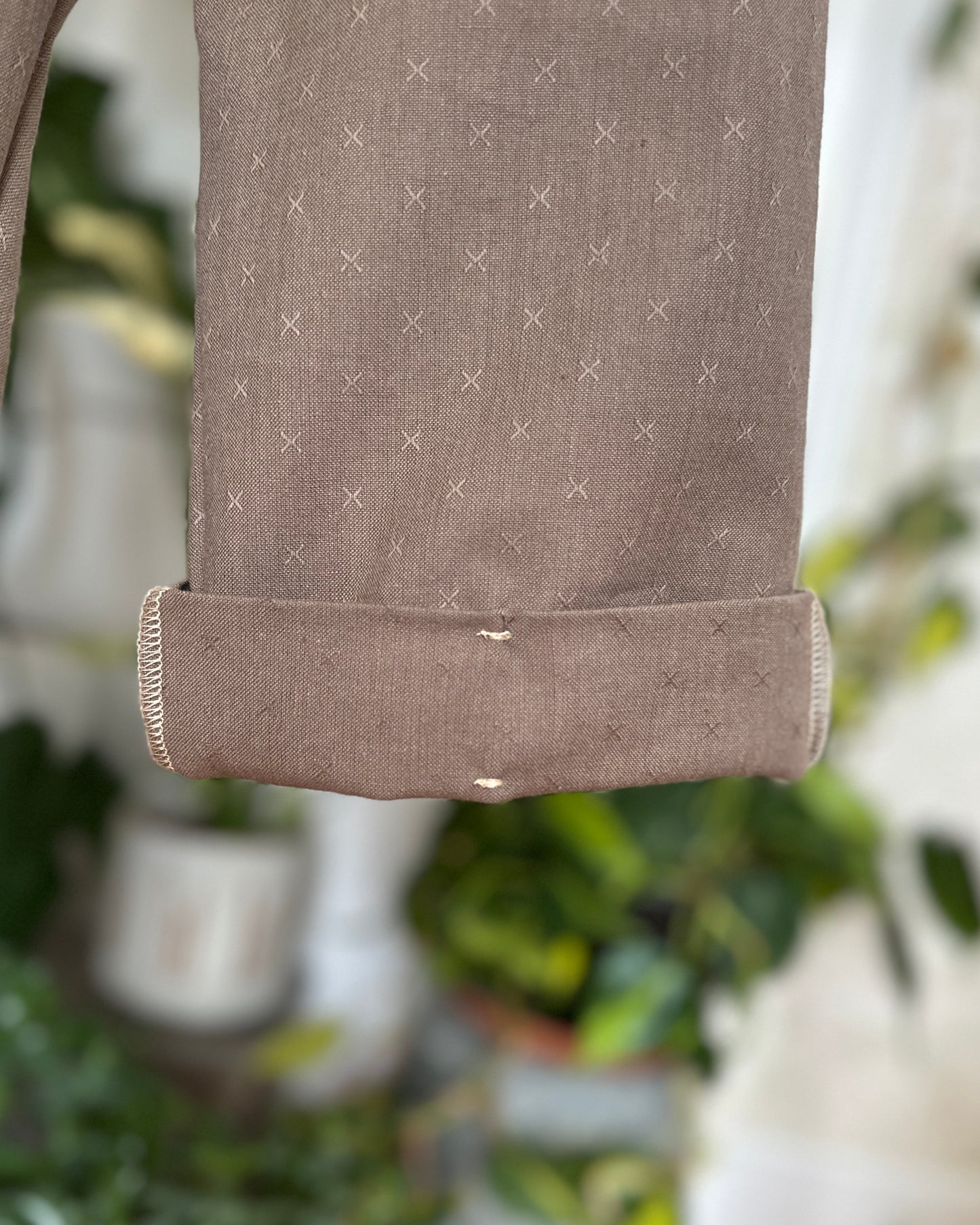 Close-up of a cuff on River Rock Caterpillar Pant with stitch detail. with a subtle pattern, blurred greenery in the background
