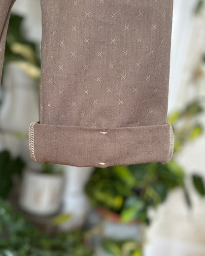 Close-up of a cuff on River Rock Caterpillar Pant with stitch detail. with a subtle pattern, blurred greenery in the background