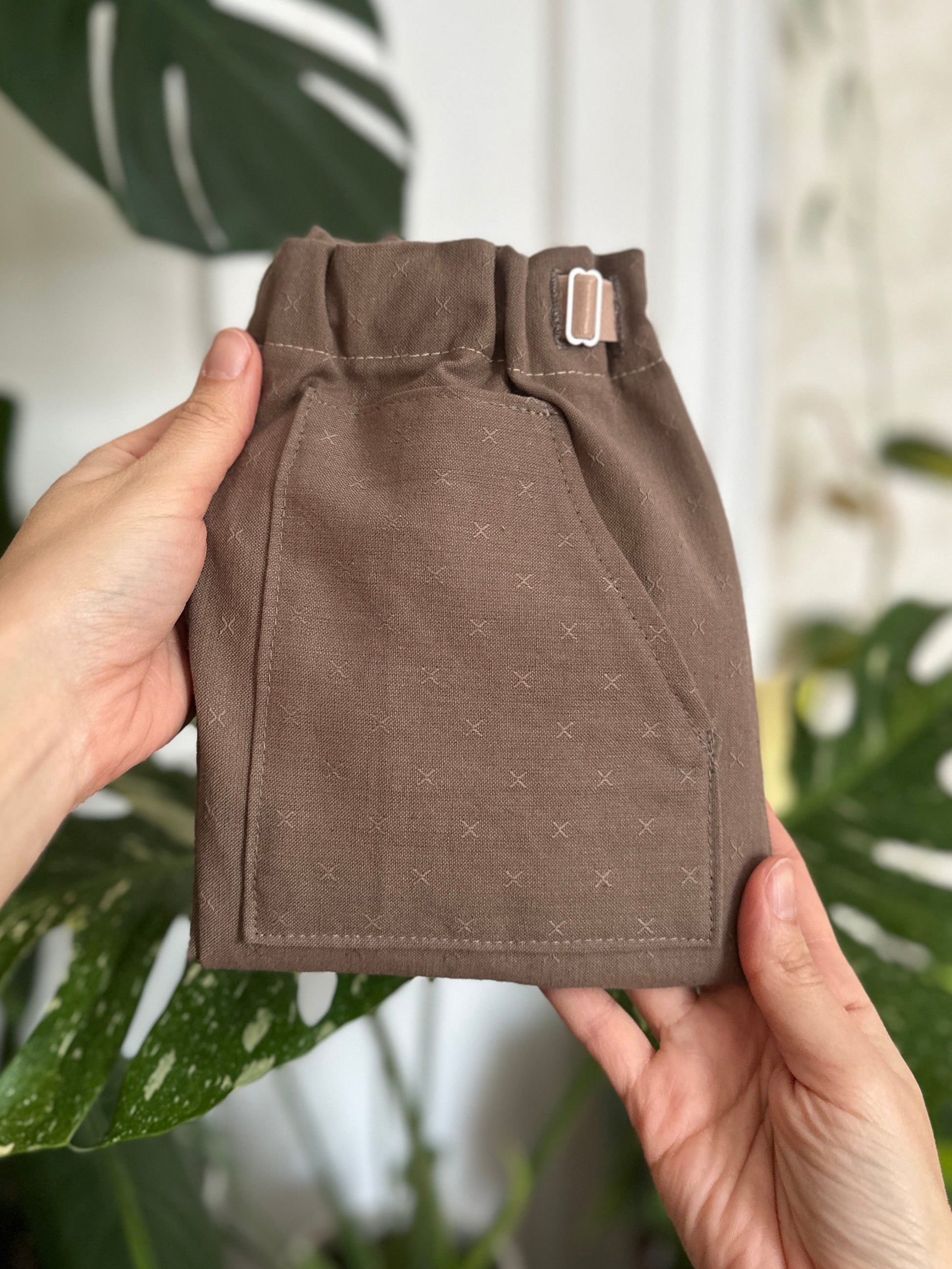 River Rock Caterpillar Pants held by a person with plants in front of blurry plant background