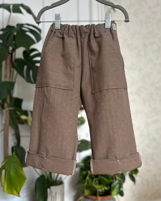 Brown pants hanging on a hanger with a blurred plant background