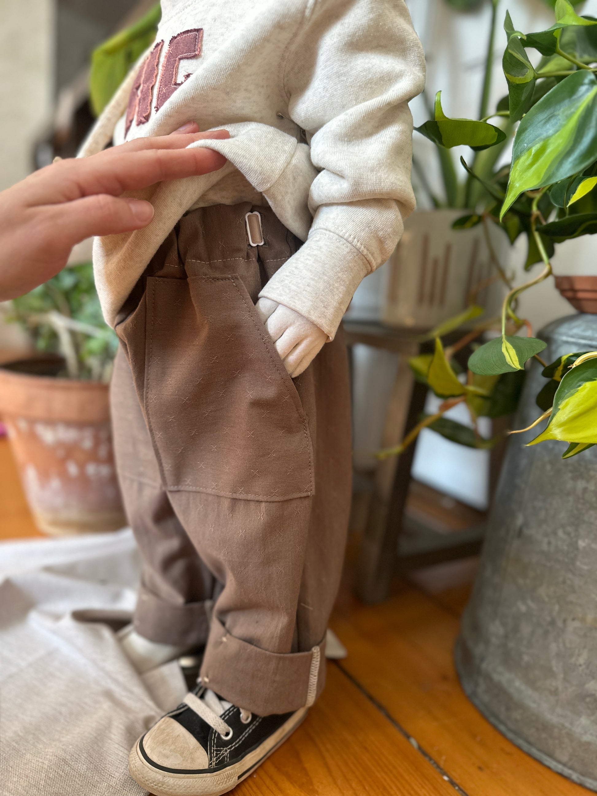 Child wearing a grey sweatshirt and River Rock Caterpillar Pants with a focus on adjustable waistband with a blurred indoor background