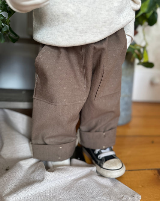 child mannequin wearing brown pants and a white sweater with a blurred background