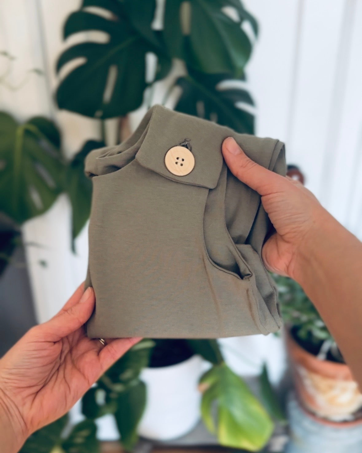 Willow green romper folded held by hands with wooden button against a blurry background