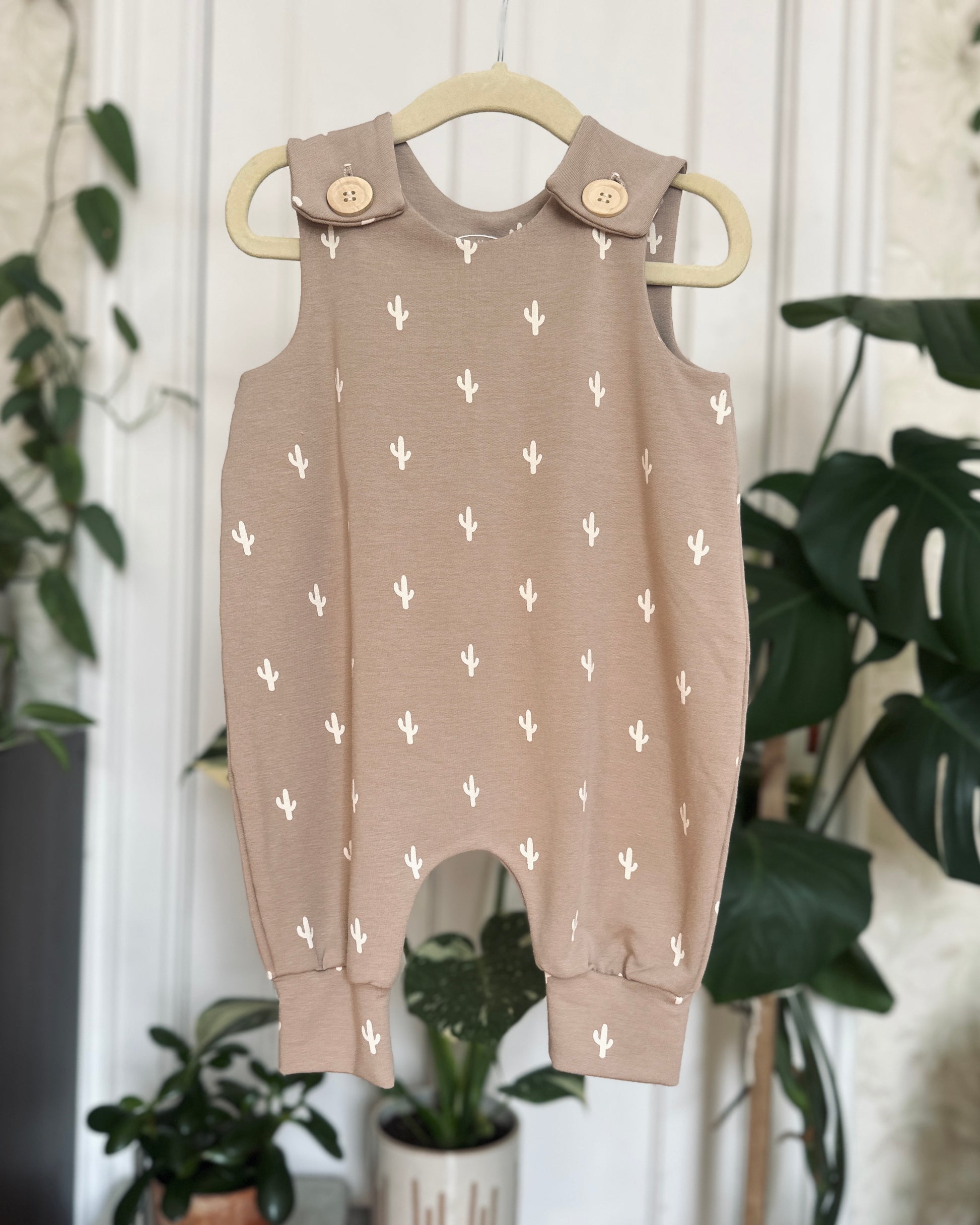 grey with white cactus print romper hanging from hanger in front of blurred plant background